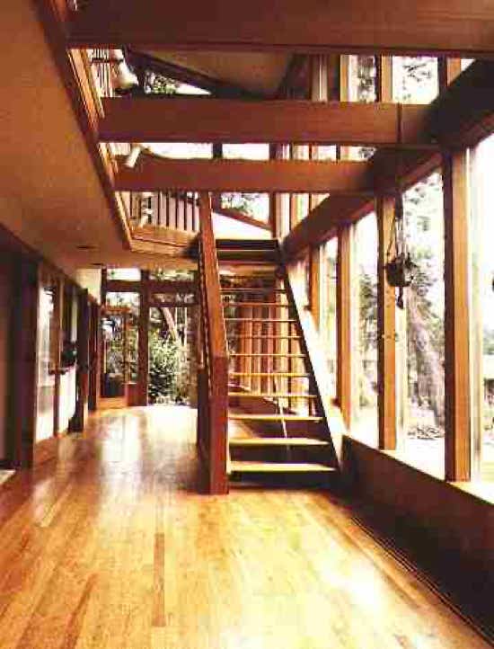 A sunroom hallway lit by tall windows, with a wooden stair and a fir floor